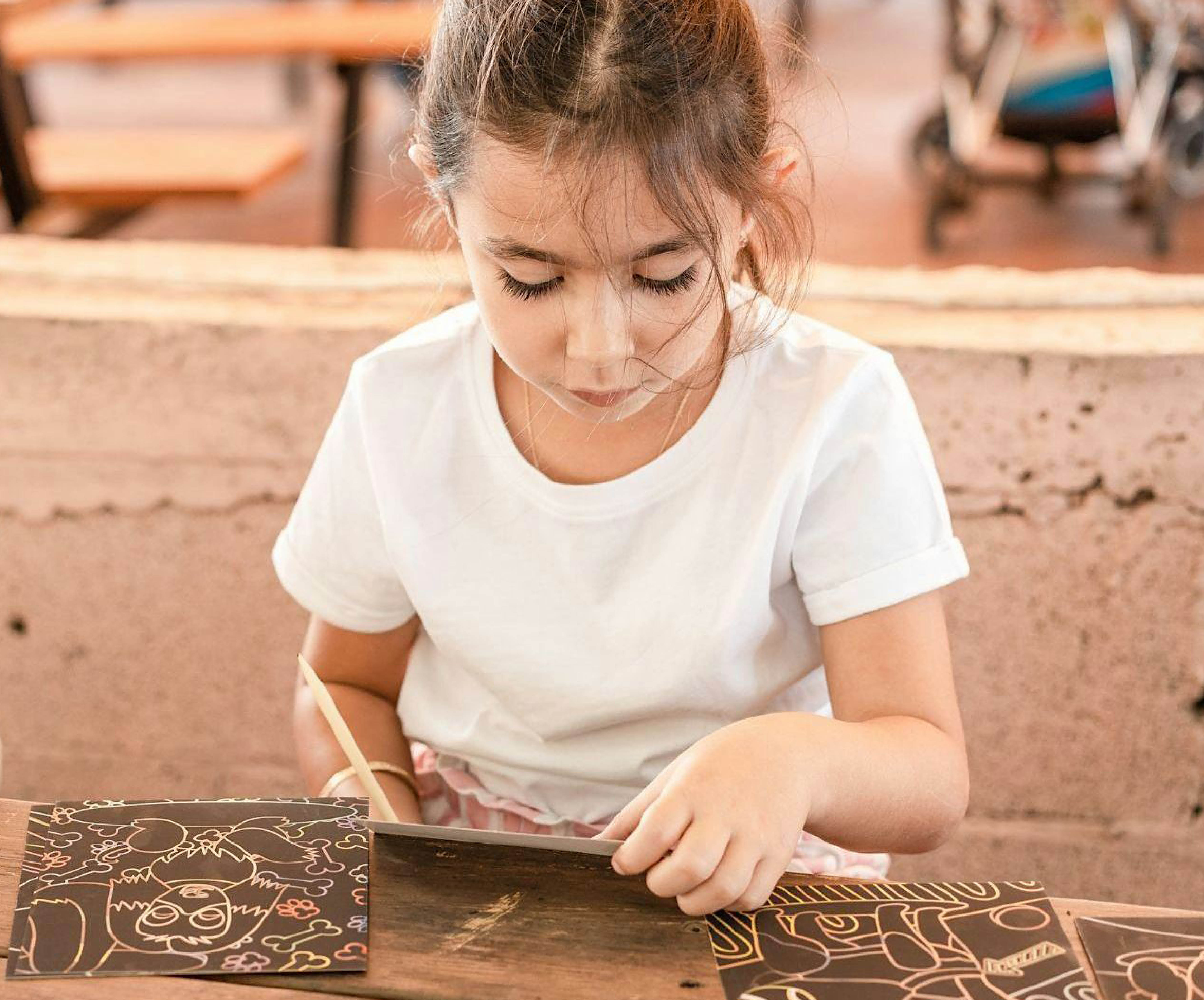 Young girl in white tshirt working on scratch board craft