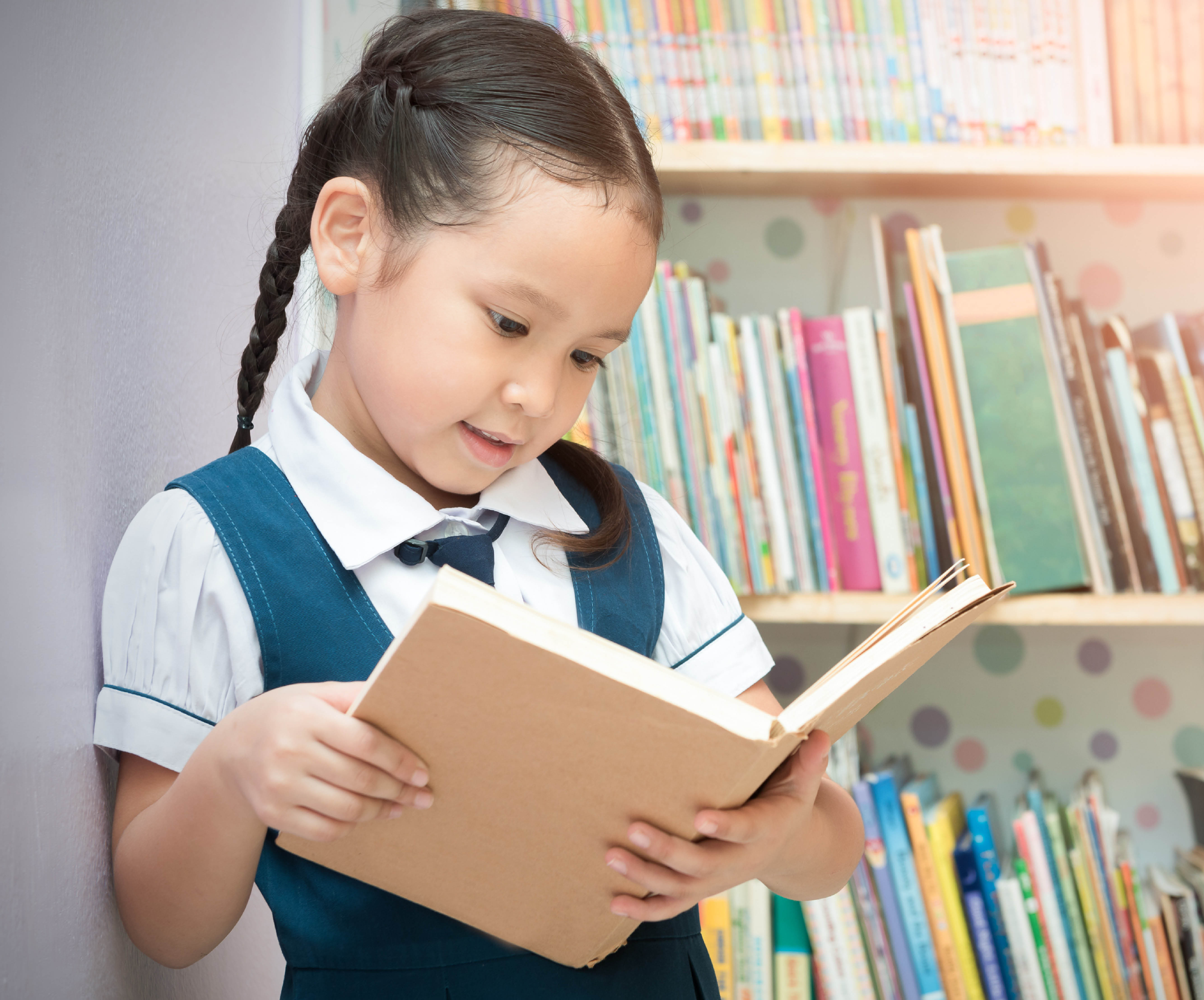 young girl reading book by shelves wearing what looks like a uniform