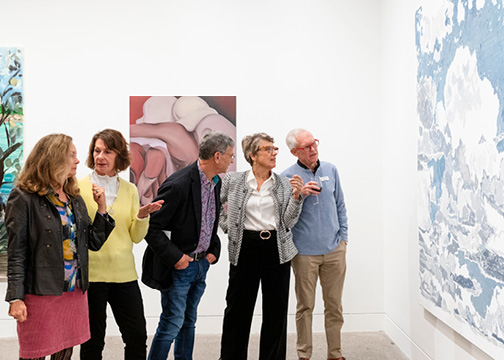 A group of five people in an art gallery looking at and discussing a painting.