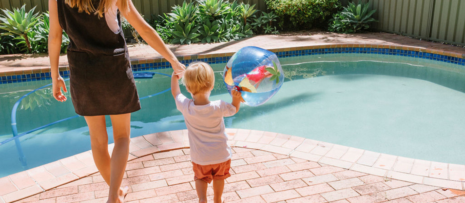 Woman holding a child's hand near a swimming pool