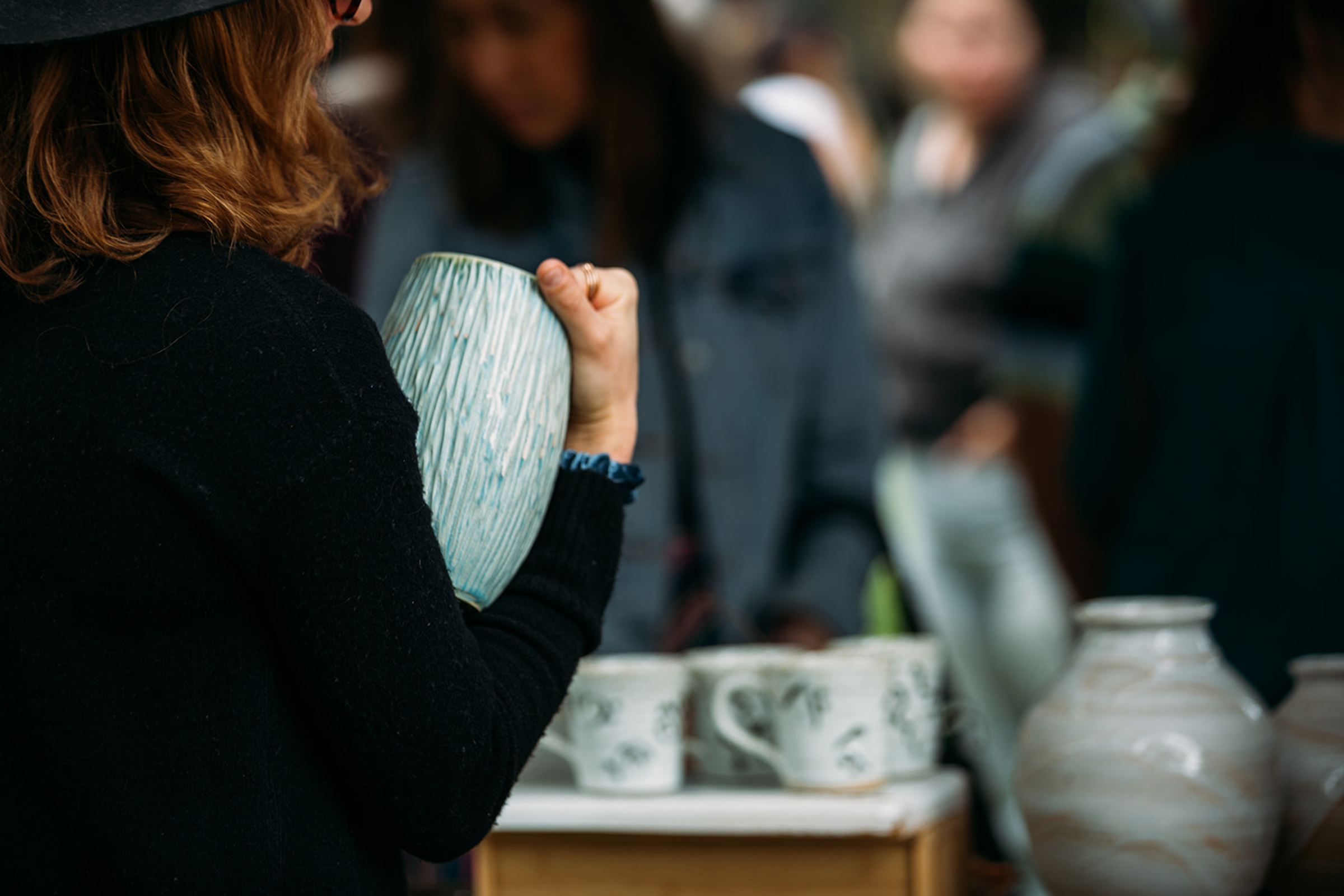 Woman holding ceramic vase in market setting.