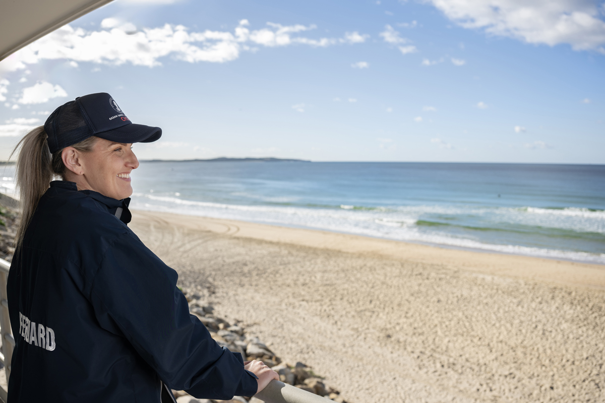 Woman in a lifeguard uniform standing watching the beach from a high vantage point.