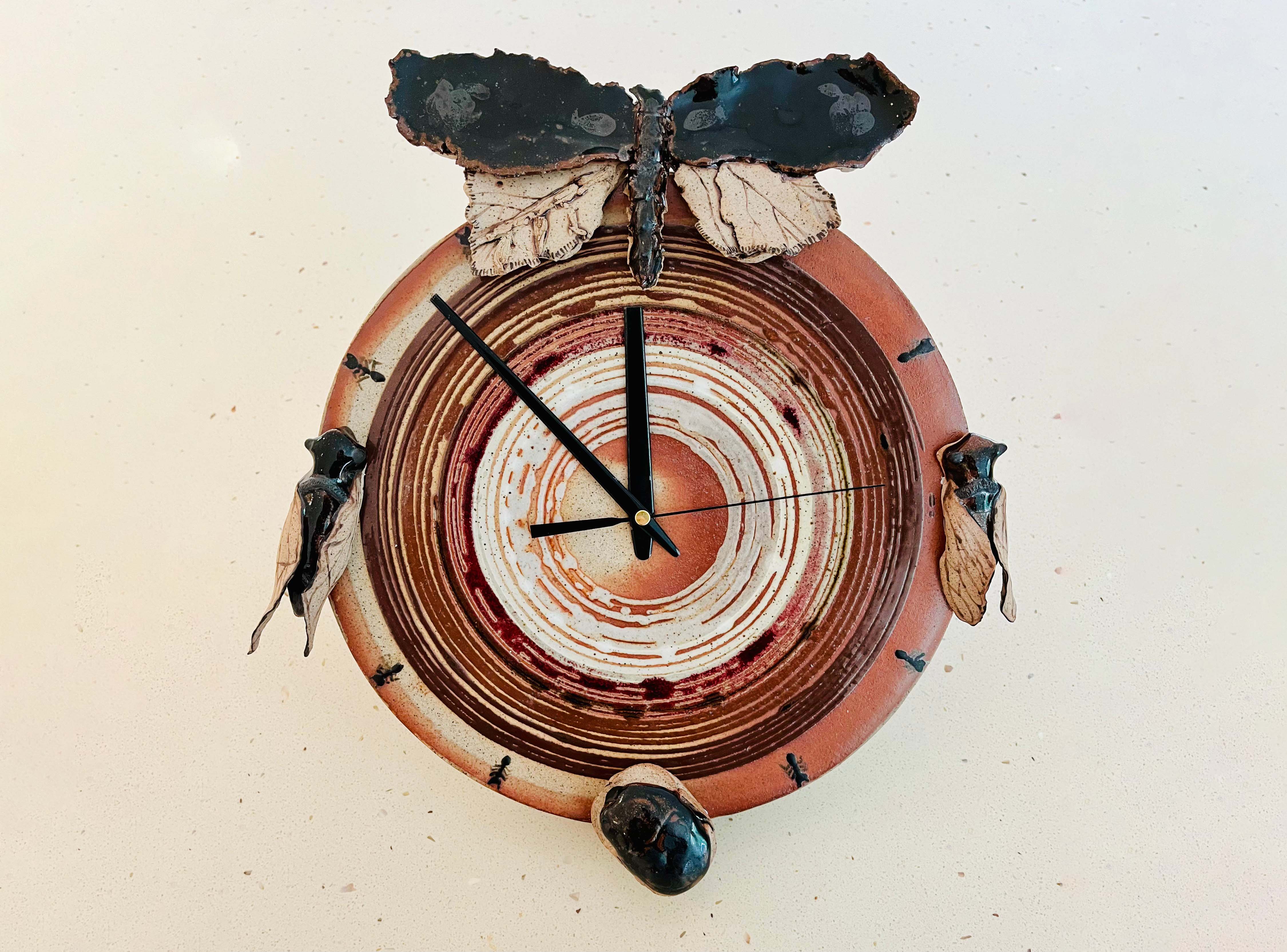 A clockface mad from ceramic with ants, cicadas and a winges insect also made from clay adorning it.