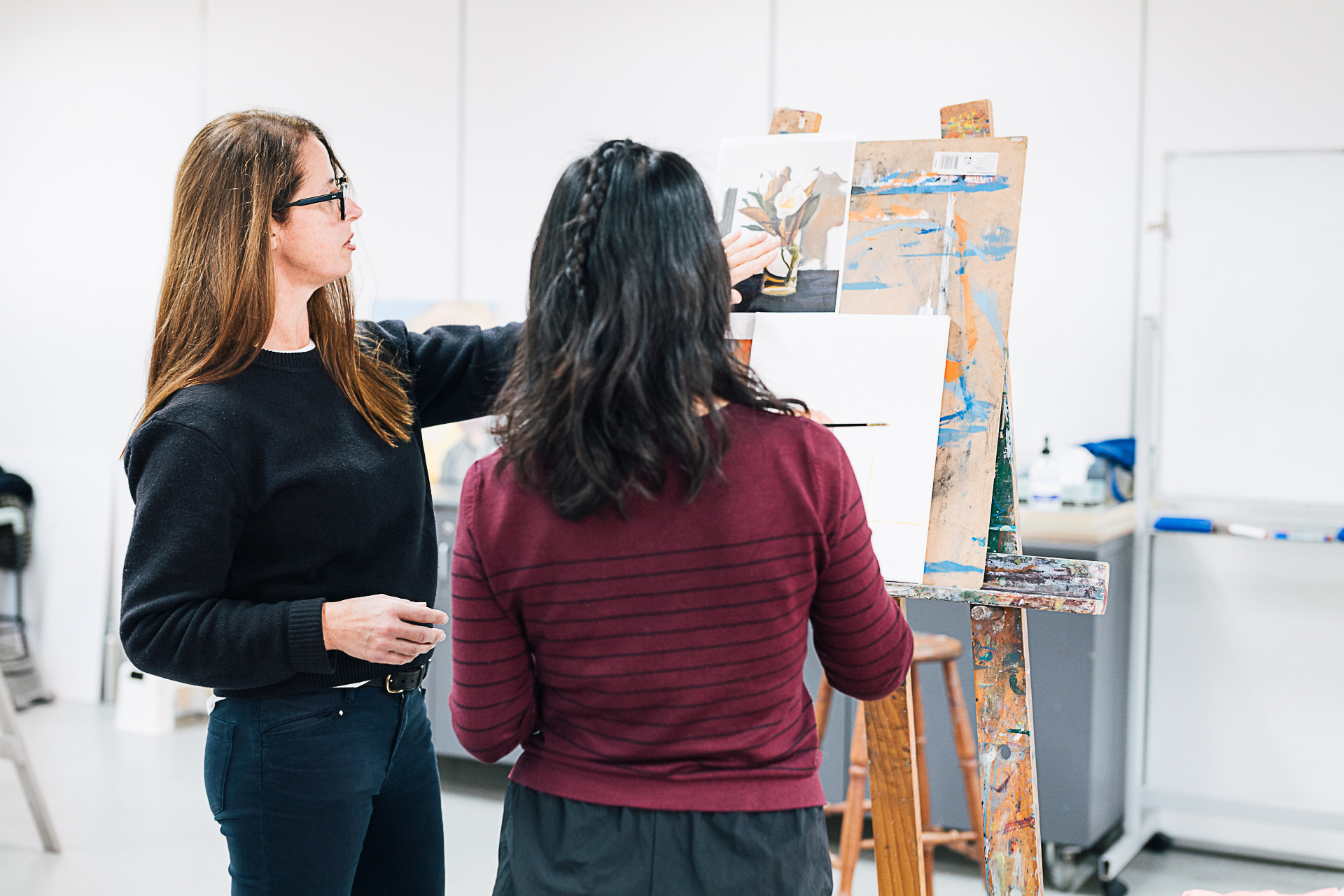 Female teacher instructing female student at painters easel in an art studio.