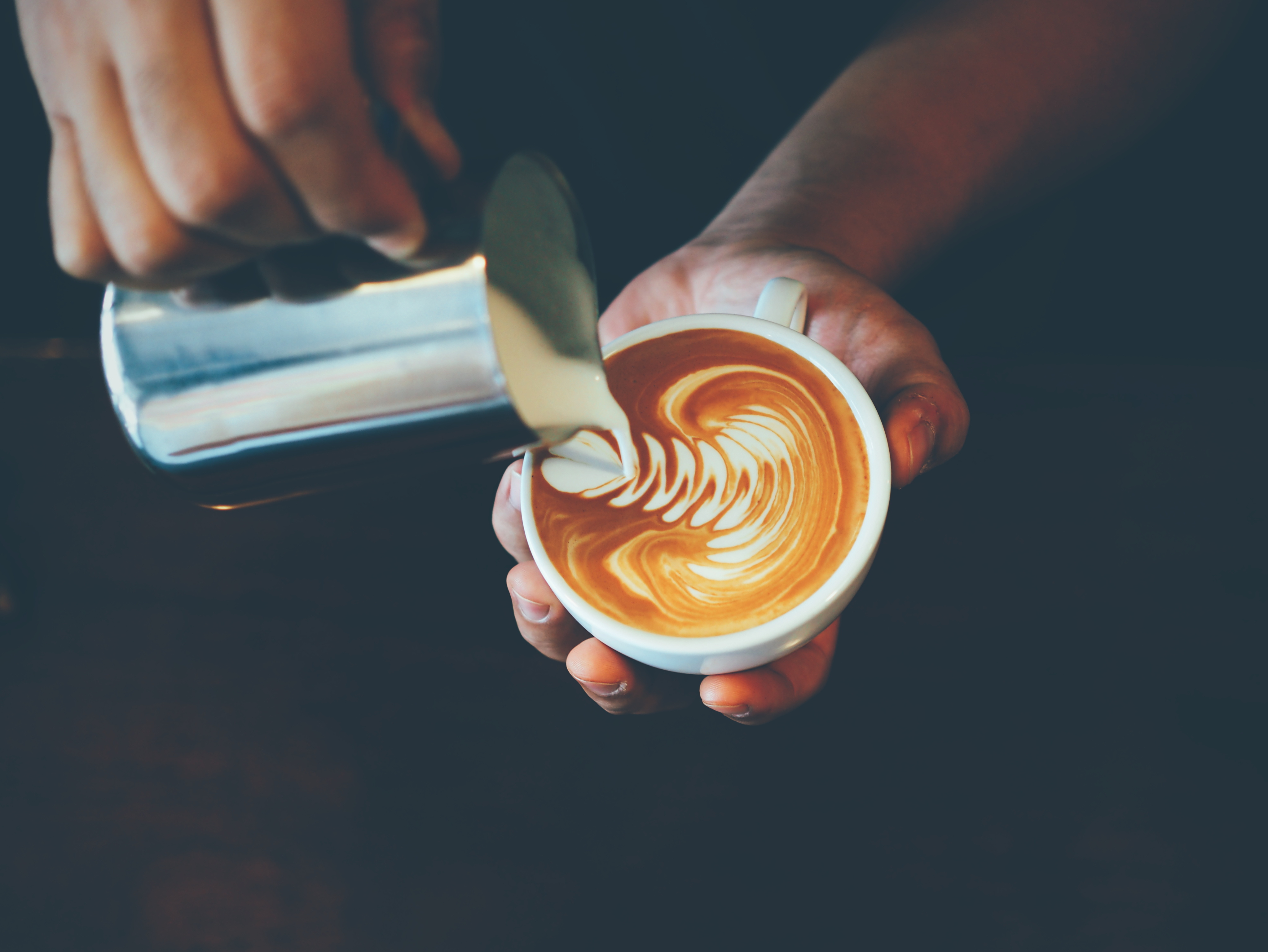 A close up photograph of a barista's hands pouring a latte.