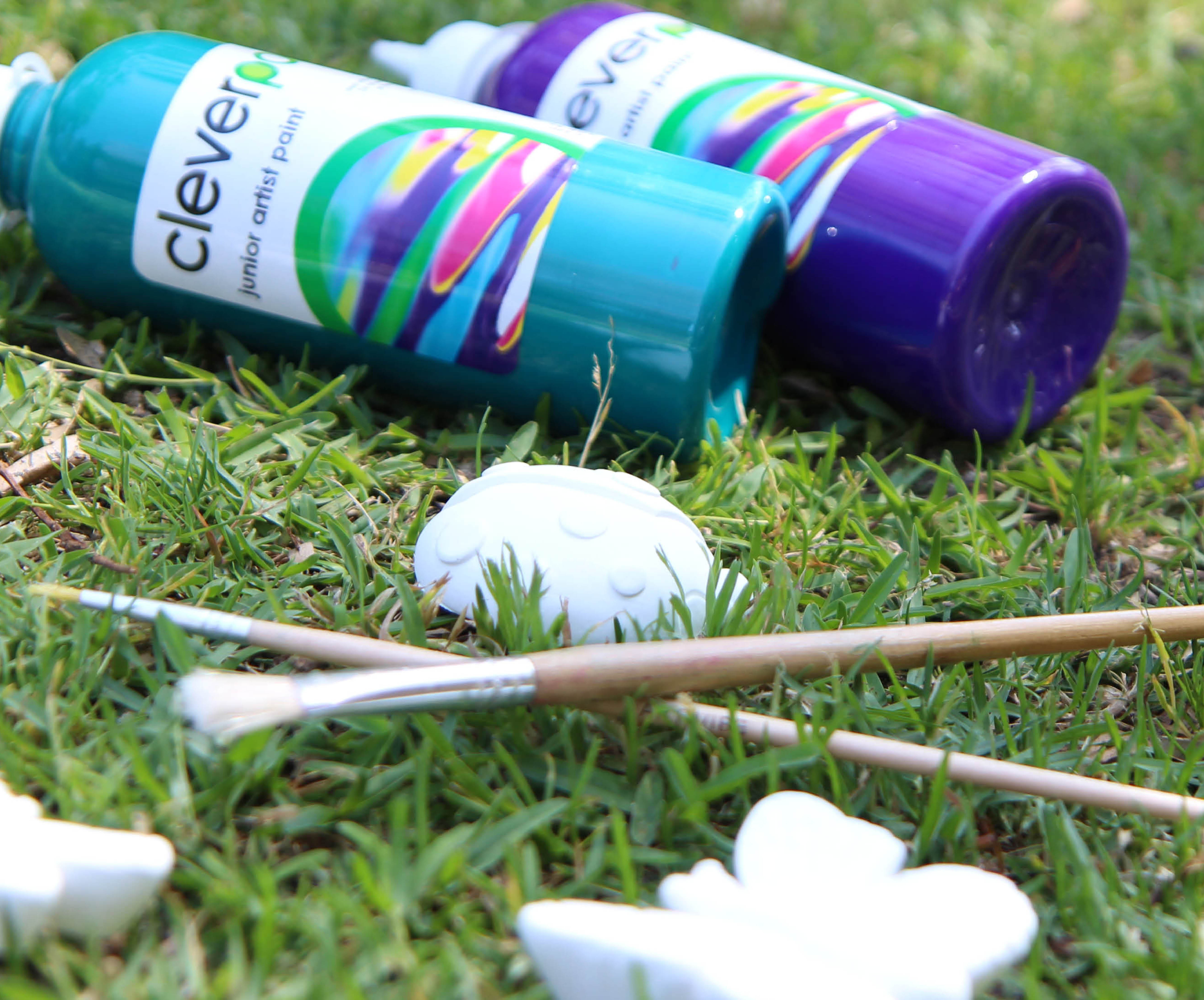 two paint pots and paint brushes with porcelain animal on the grass