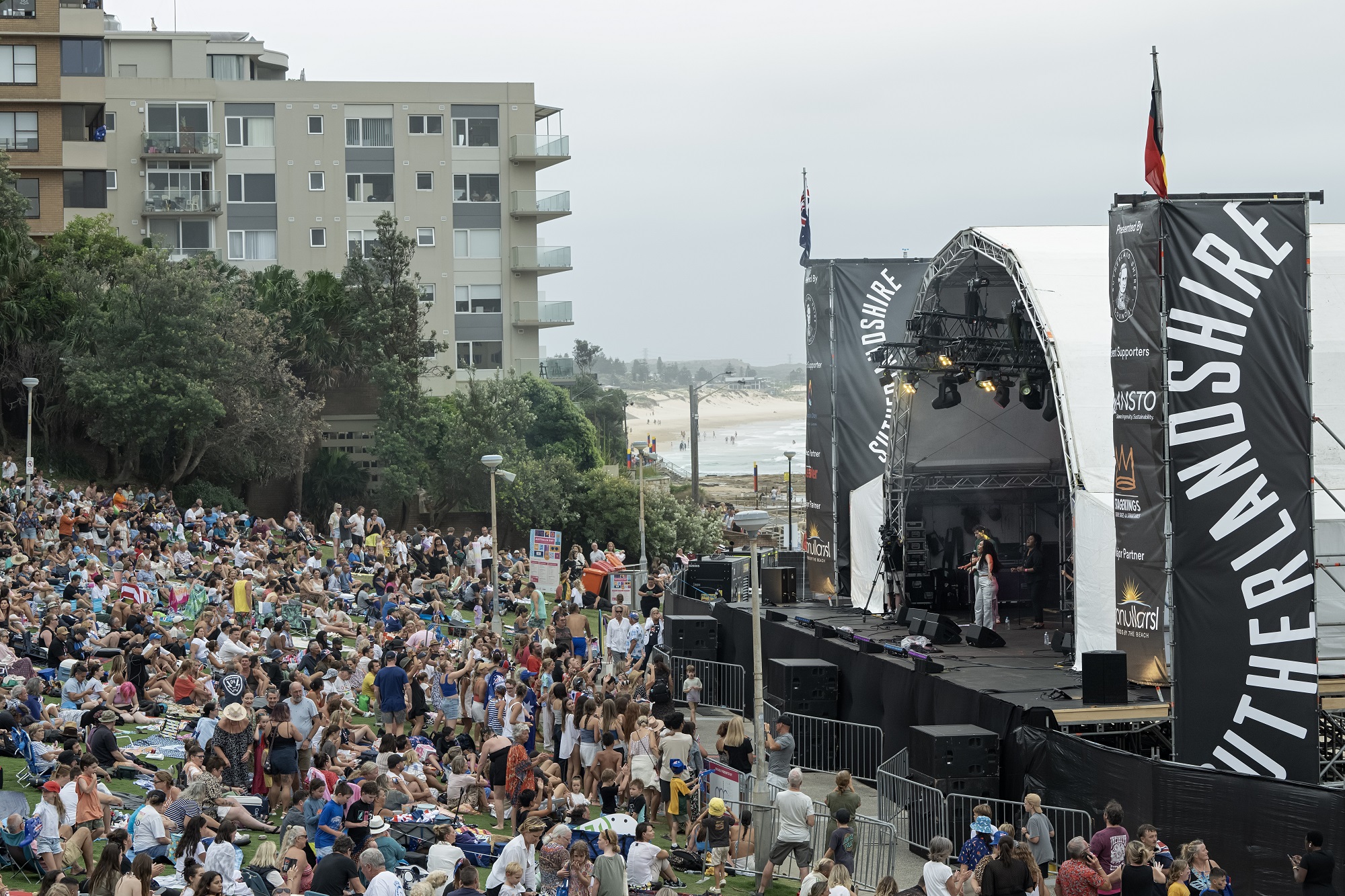 Crowd sitting in front of an outdoor stage at Cronulla Park