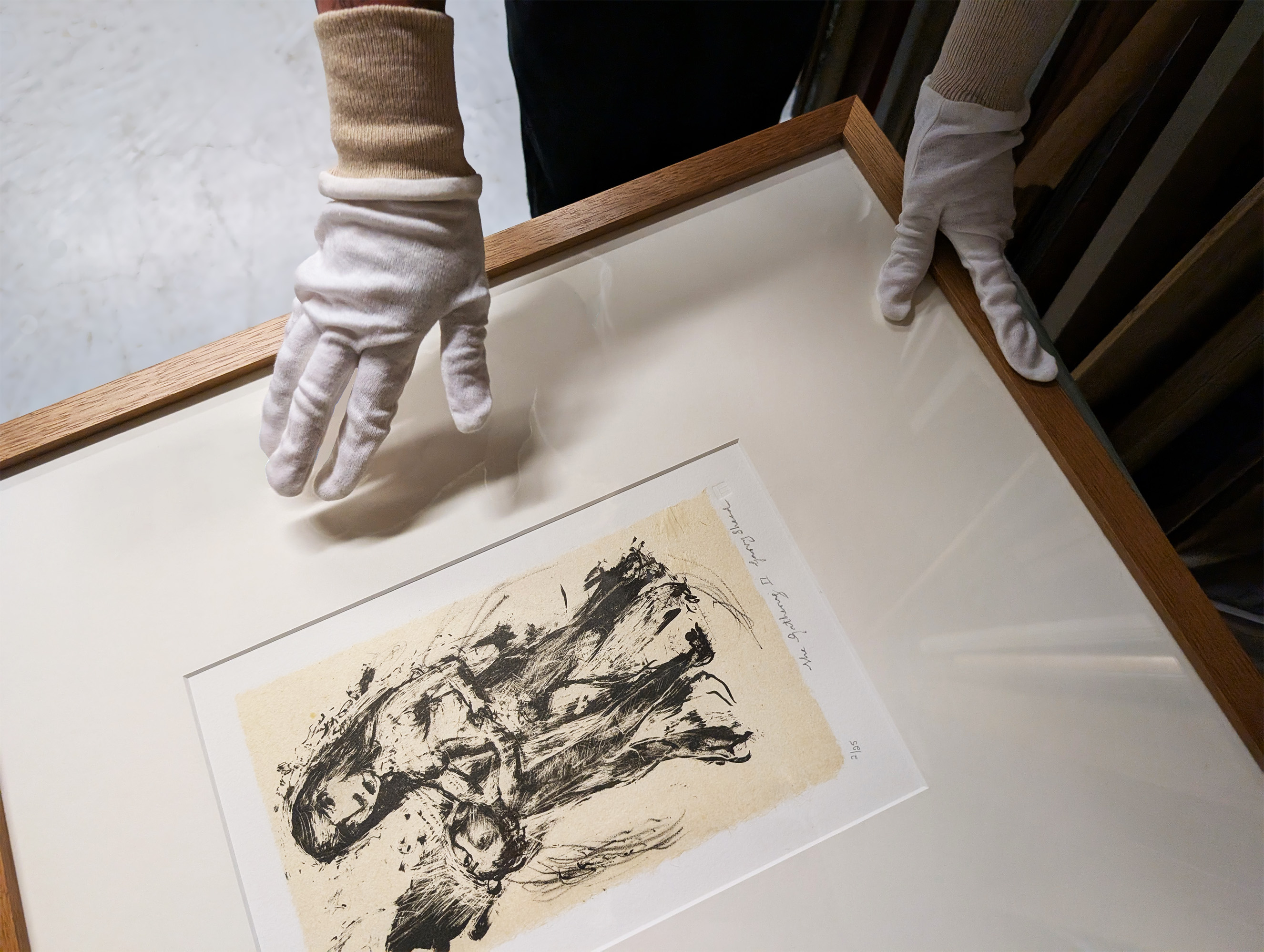 Hands wearing white cotton gloves holding a framed artwork.