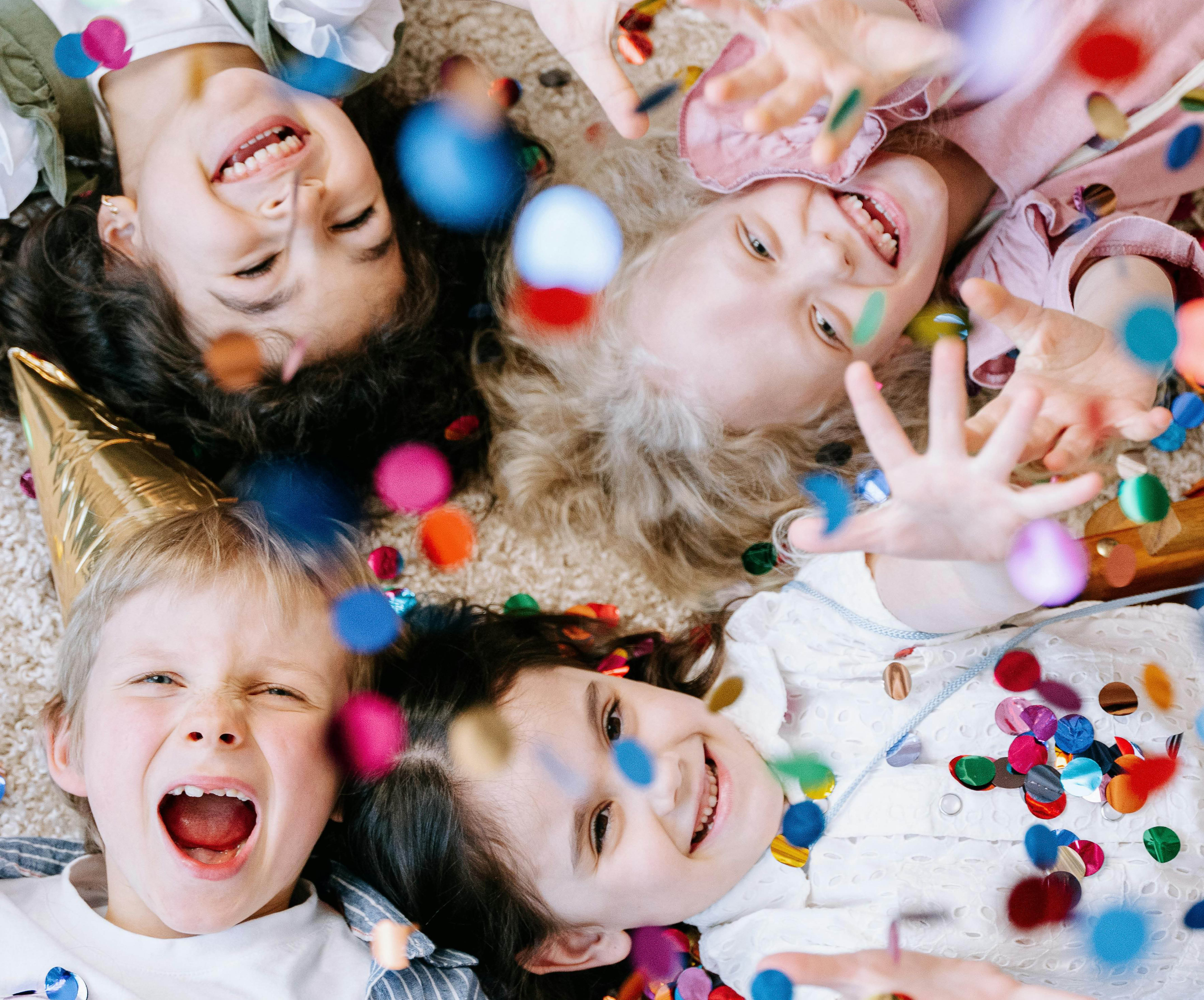 four laughing children laying on the floor covered in confetti