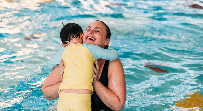 Mum smiling and hugging their child in the water.