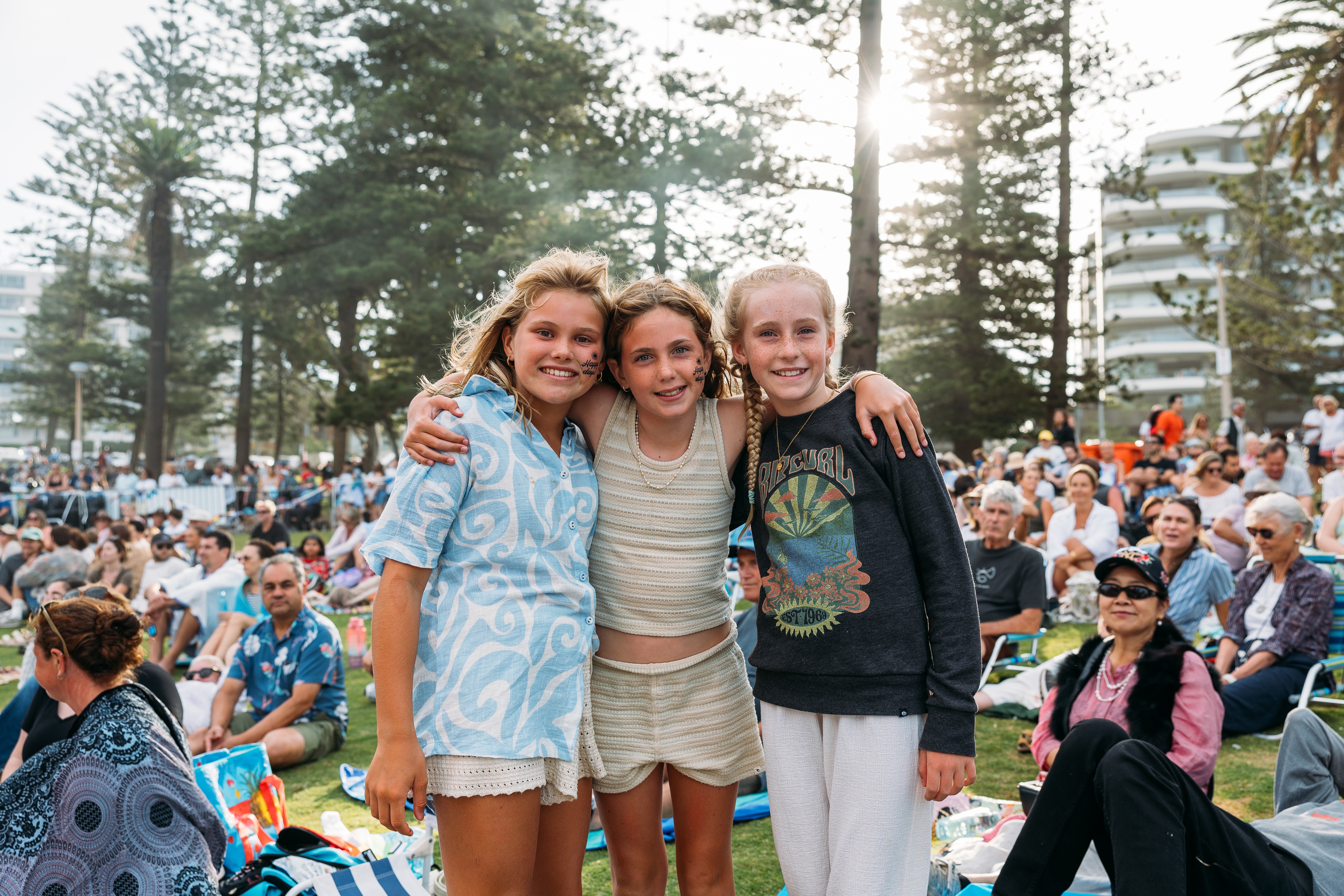 Three girls posing together and smiling at Australia Day concert, crowd in background