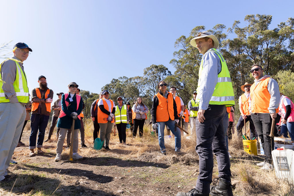 A group of people in fluoro vests standing outdoors with trees in the background