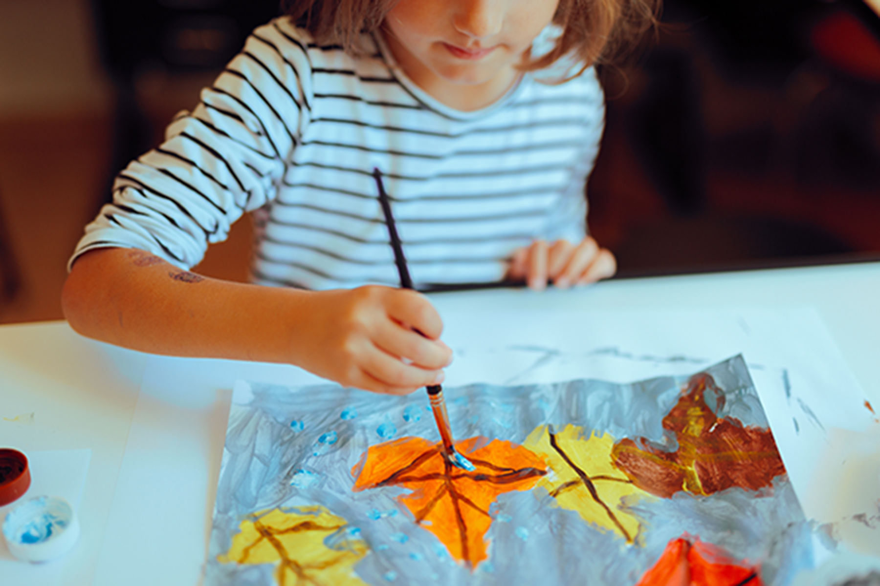 A school aged girl wearing a pink skivvy and paint smock painting on an easel.