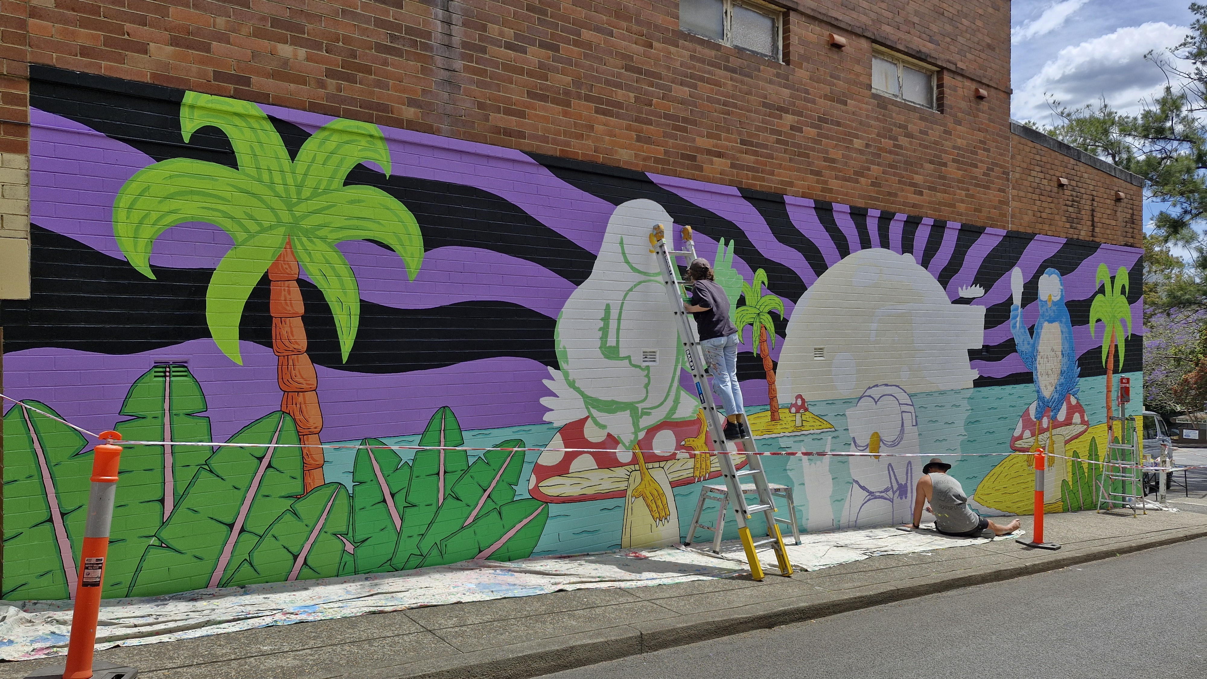 Mulga (artist Joel Moore) painting a mural on a large brick wall